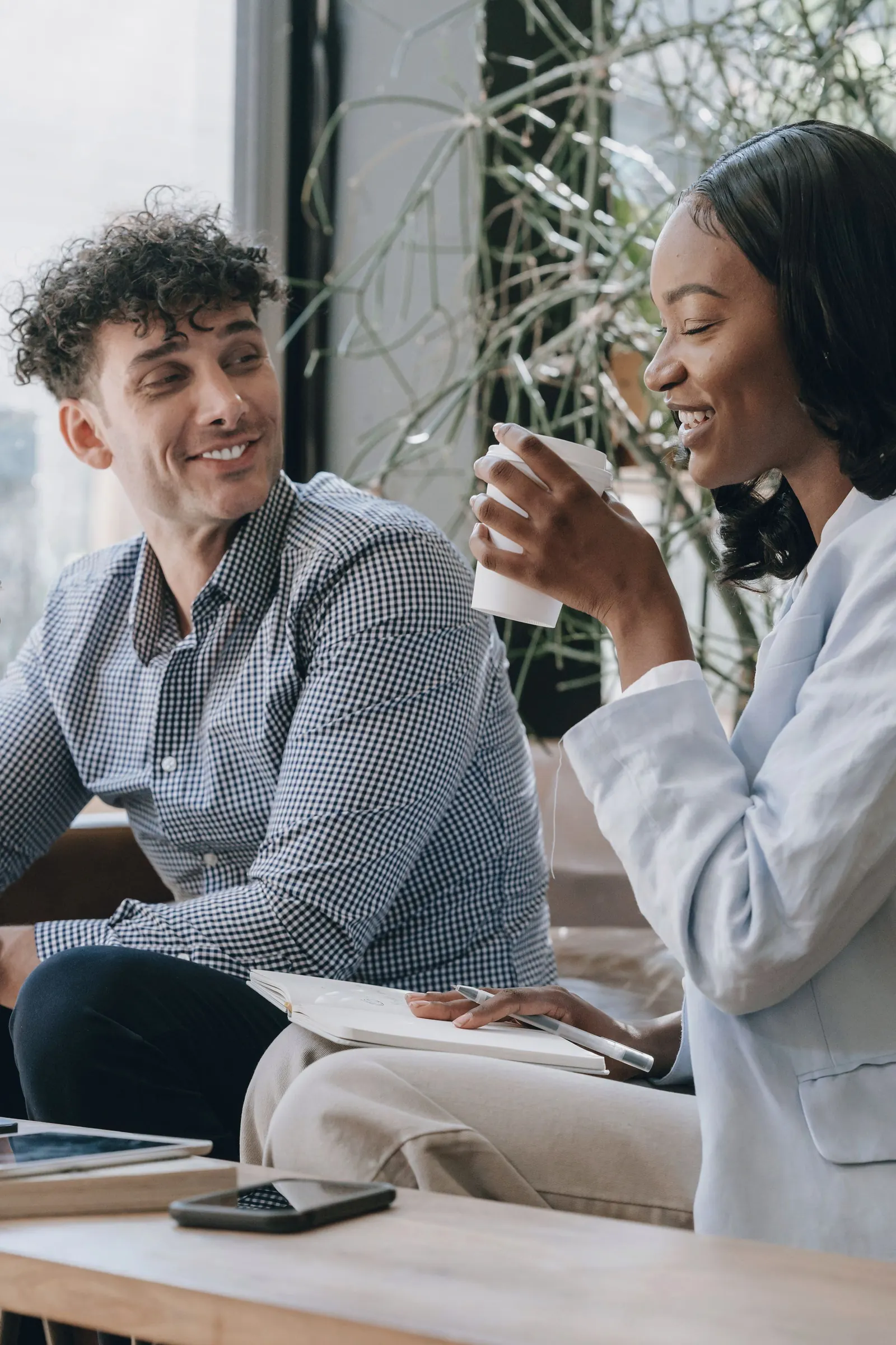 Two colleagues laugh over coffee at a shared table.